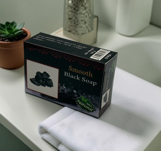 Box of Smooth Black Soap on a bathroom counter with a white towel and plant in the background