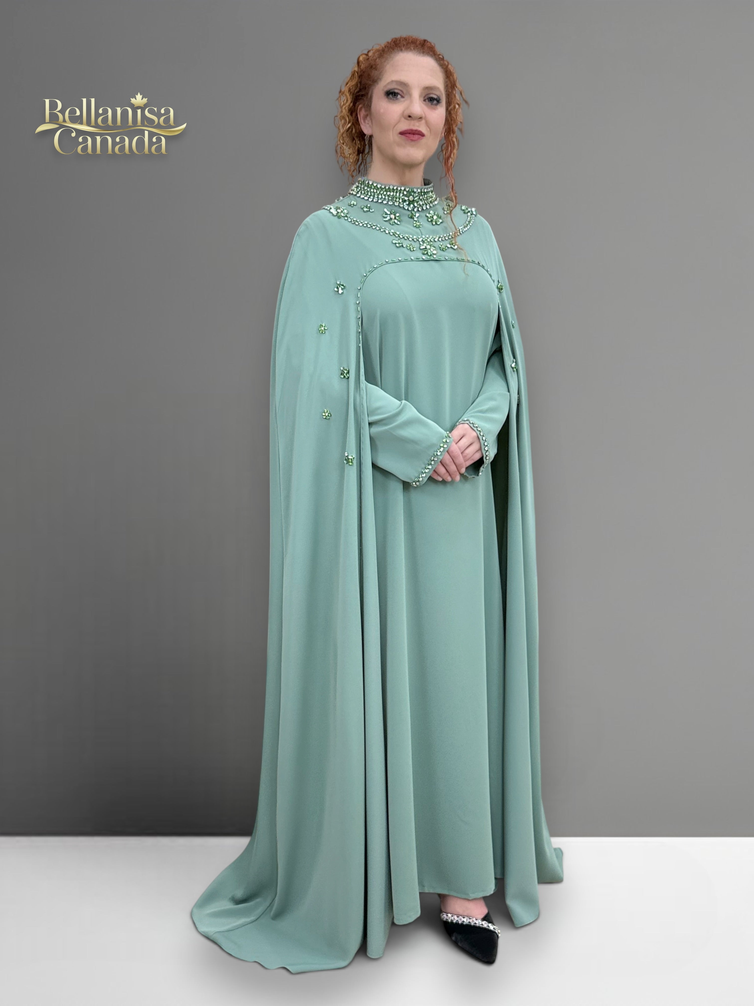 Woman wearing a light green dress with a cape and embellishments, standing against a gray background. Brand 'Bellanisa Canada' is visible.