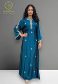 Woman wearing a blue dress with embroidery, standing against a gray background with Bella Nisa branding.
