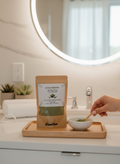 Bellanisa Qasil Powder face and body mask in a brown pouch, with green powder in a small bowl and a wooden spoon.